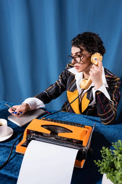Brunetta newswoman in vintage blazer holding penna mentre parla al telefono su sfondo blu — Foto stock