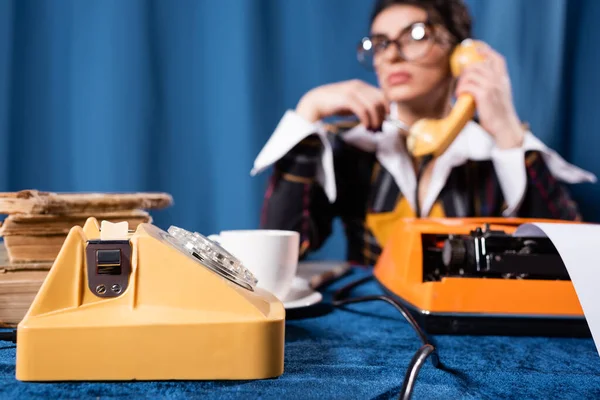 Selektiver Fokus eines alten Telefons in der Nähe einer verschwommenen Nachrichtensprecherin, die auf blauem Hintergrund spricht — Stockfoto