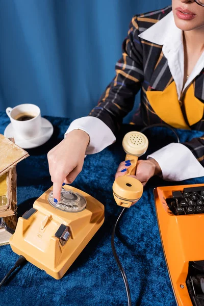 Vista parcial de la mujer con estilo que llama por teléfono cerca de la máquina de escribir y taza de café sobre fondo azul - foto de stock