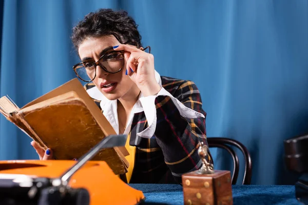 Vintage style newswoman in eyeglasses reading book on blue background — Stock Photo