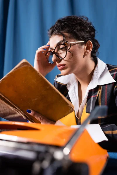 Stilvolle Frau mit Brille liest Vintage-Buch auf blauem Hintergrund — Stockfoto