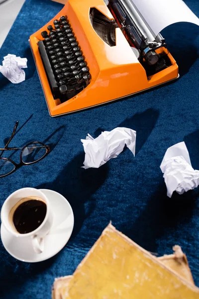 Top view of coffee cup near vintage typewriter, eyeglasses and crumpled paper on blue velour tablecloth — Stock Photo