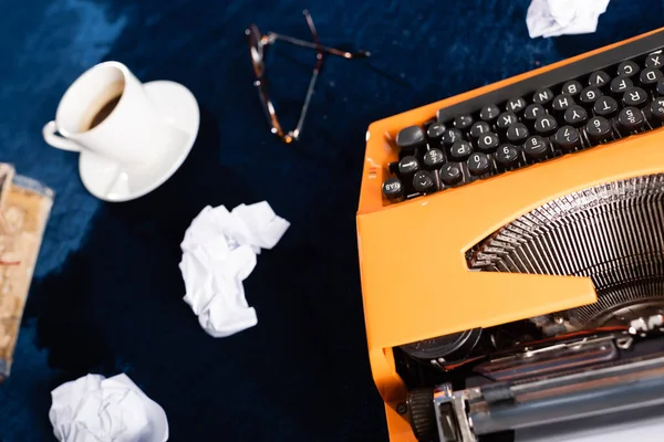Vista superior da máquina de escrever retro, papel amassado e xícara de café borrada na mesa azul — Fotografia de Stock