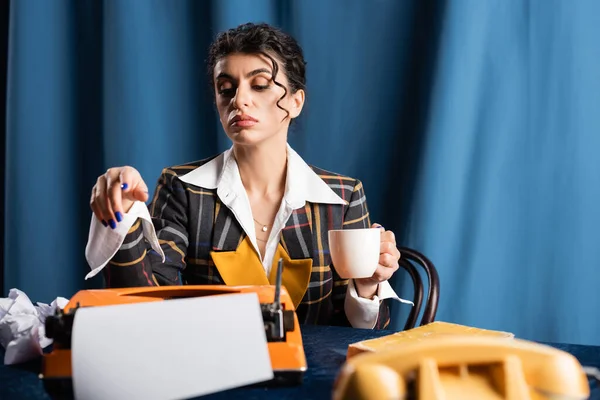 Jornalista elegante com xícara de café perto de máquina de escrever vintage em fundo azul — Fotografia de Stock