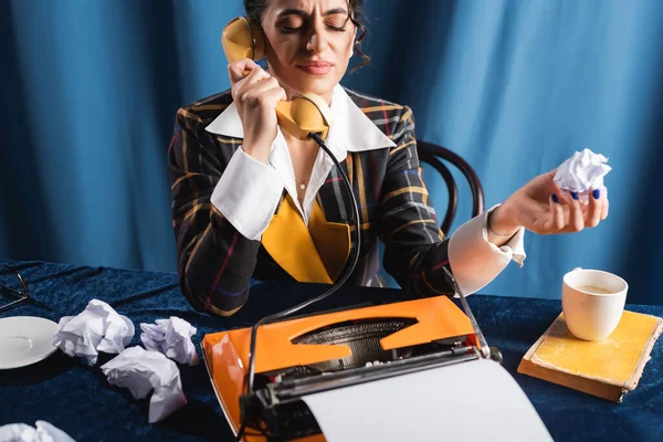 Femme mécontente avec les yeux fermés tenant papier froissé et parlant au téléphone sur fond bleu — Photo de stock