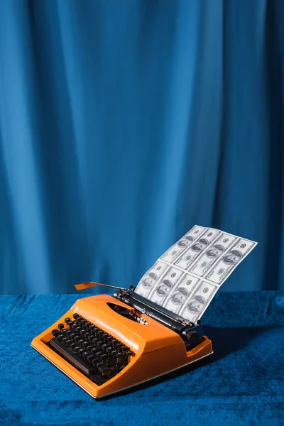 Machine à écrire vintage rouge avec des dollars sur table en velours près drapé bleu sur fond — Photo de stock