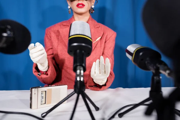 Micrófonos cerca de recortado estilo vintage mujer dando entrevista sobre fondo azul - foto de stock