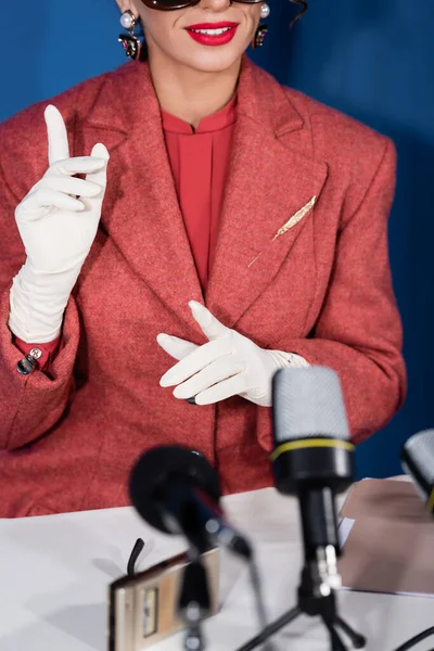 Partial view of vintage style woman pointing with fingers near microphones during interview of blue background — Stock Photo