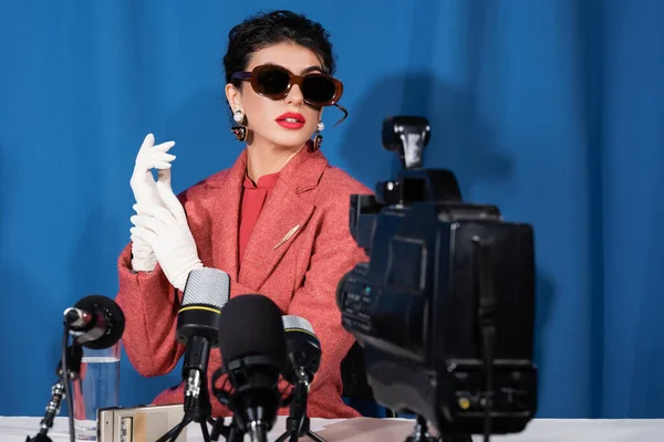 Câmera de vídeo borrada e microfones perto de mulher estilo retro dando entrevista no fundo azul — Fotografia de Stock