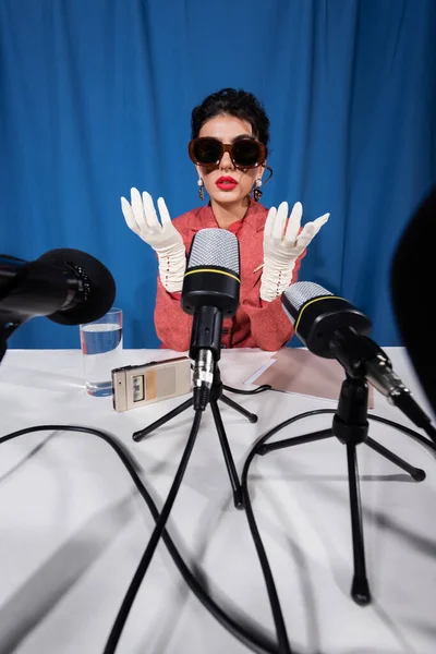 Stile vintage donna in guanti bianchi vicino registratore vocale e microfoni su sfondo blu — Foto stock