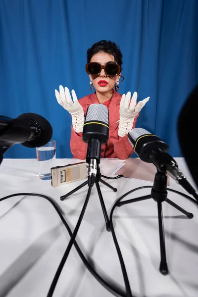 Vintage style woman in white gloves near voice recorder and microphones on blue background — Stock Photo