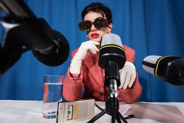 Micrófonos cerca de vidrio de agua, grabadora de voz y mujer de estilo vintage sobre fondo azul - foto de stock