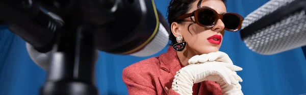 Vue rapprochée de microphones flous près de la femme dans des lunettes de soleil vintage sur fond bleu, bannière — Photo de stock
