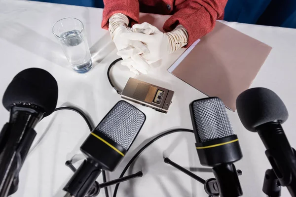 Vista parziale della donna in guanti bianchi, microfoni e registratore vocale su tavolo bianco — Foto stock