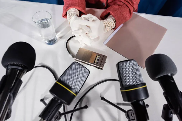 Partial view of woman in white gloves, microphones and voice recorder on white table — Stock Photo