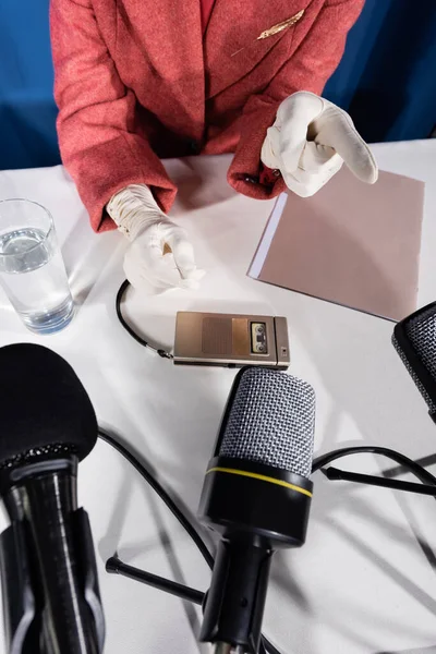 Ansicht von oben von beschnittener Frau in weißen Handschuhen, die mit dem Finger in die Nähe von Mikrofonen und Stimmenrekorder zeigt — Stockfoto