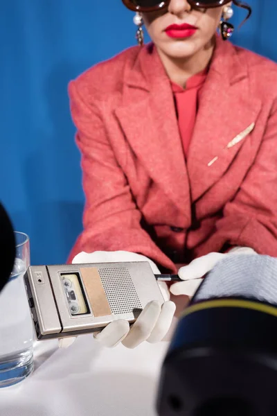 Cropped view of blurred woman holding voice recorder near blurred microphones on blue background — Stock Photo