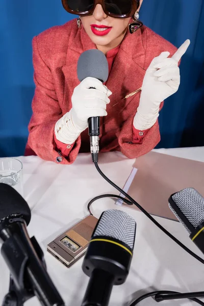 Recortado vista de la mujer de estilo vintage señalando con el dedo durante la entrevista sobre fondo azul - foto de stock