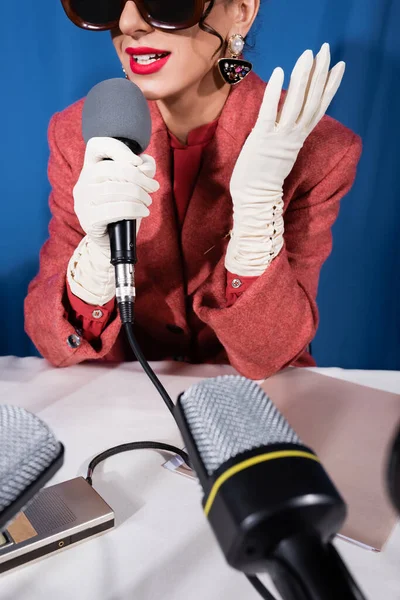 Cropped view of retro style woman speaking in microphone while giving interview on blue background — Stock Photo