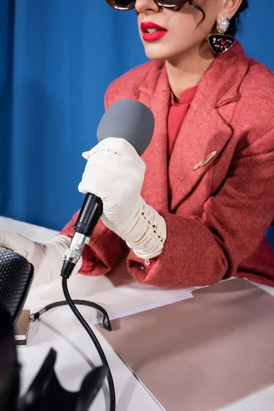 Vista ritagliata di donna elegante in guanti bianchi con microfono su sfondo blu — Foto stock