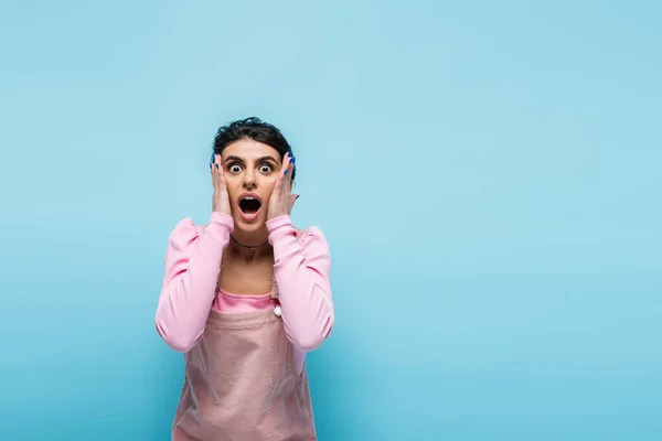 Schockierte Frau mit offenem Mund, die Hände in der Nähe des Gesichts hält, isoliert auf blauem Grund — Stockfoto