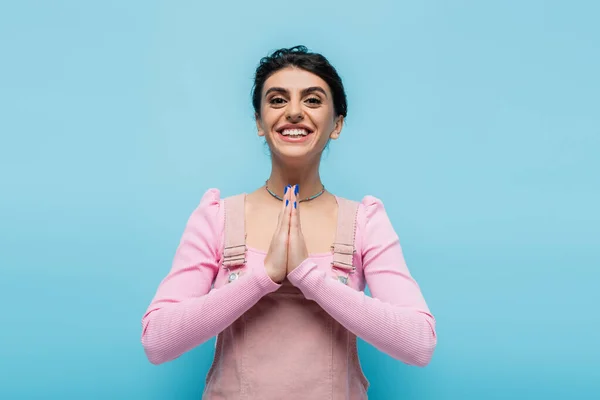 Young brunette woman showing gratitude gesture and smiling at camera isolated on blue — Stock Photo