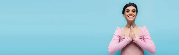 Grateful brunette woman with praying hands looking at camera isolated on blue, banner — Stock Photo