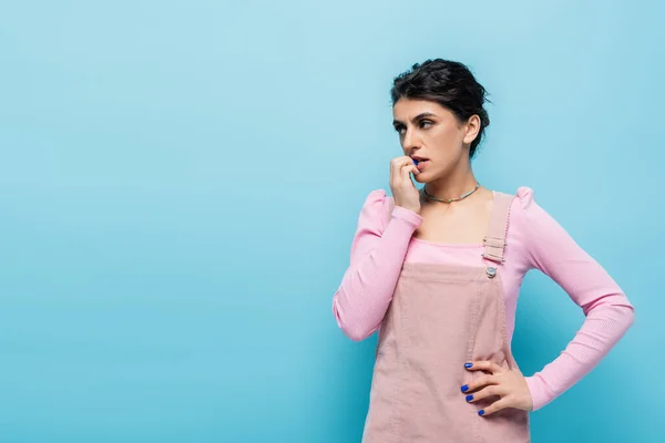 Pensive woman looking away while standing with hand on hip isolated on blue — Stock Photo