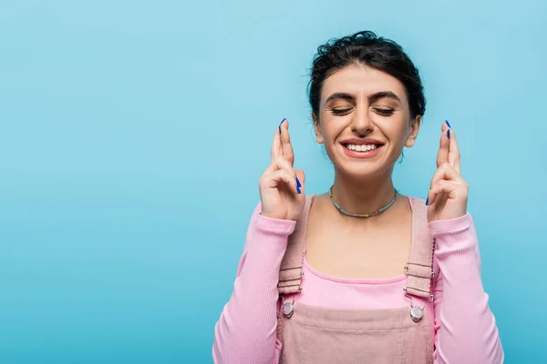 Mulher com olhos fechados e dedos cruzados sorrindo isolado em azul — Fotografia de Stock