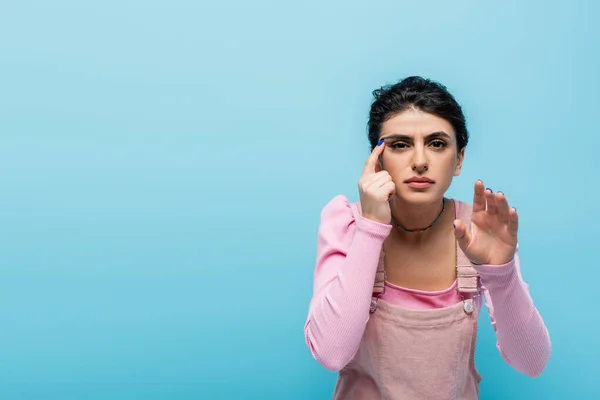 Mujer miope tocando el ojo mientras mira la cámara aislada en azul - foto de stock