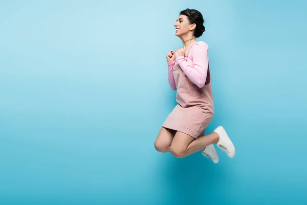 Vista completa de la mujer excitada con los puños cerrados levitando sobre fondo azul - foto de stock