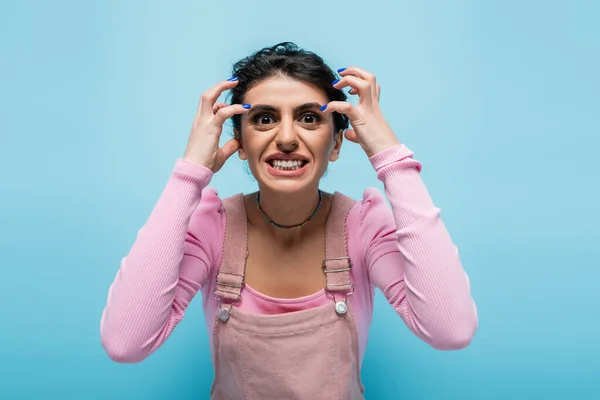 Mujer enojada haciendo muecas y gestos mientras mira la cámara aislada en azul - foto de stock