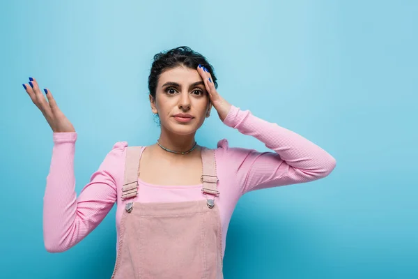 Forgetful and discouraged woman touching head while looking at camera on blue background — Stock Photo