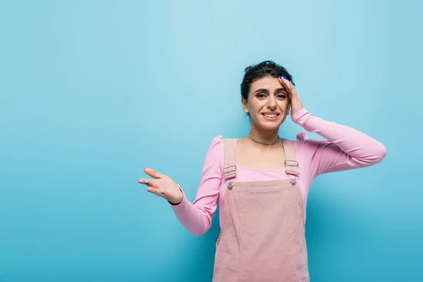 Aufgebrachte Frau berührt Kopf und zeigt mit der Hand auf blauen Hintergrund — Stockfoto