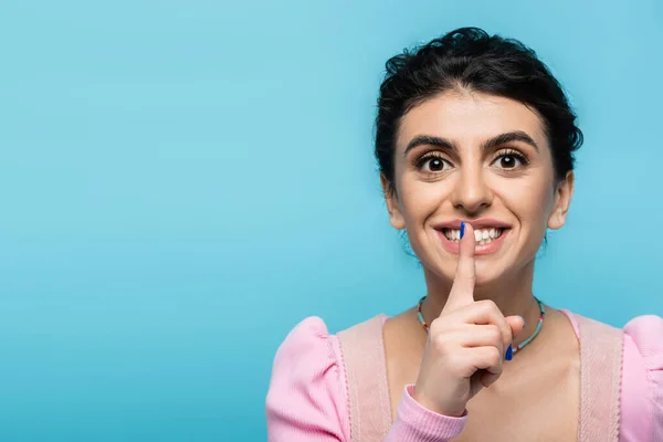 Excited woman showing hush gesture while looking at camera isolated on blue — Stock Photo