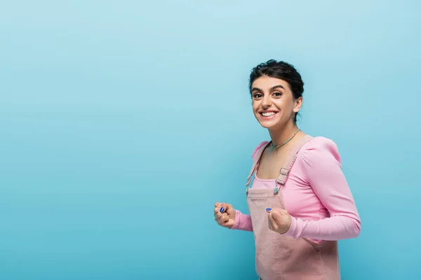 Mulher morena positiva segurando os punhos apertados para a sorte isolada no azul — Fotografia de Stock