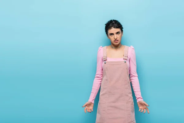 Vista frontale della donna frustrata in abiti alla moda guardando la fotocamera isolata sul blu — Foto stock