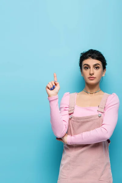 Young and stylish woman pointing up with finger on blue background — Stock Photo