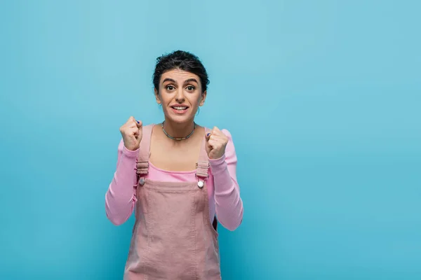 Hopeful and positive woman holding clenched fists for luck isolated on blue — Stock Photo