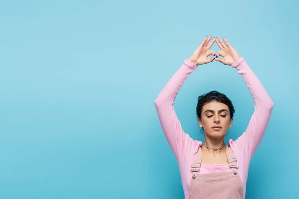 Young woman with closed eyes meditating with raised hands and jnana mudra gesture isolated on blue — Stock Photo