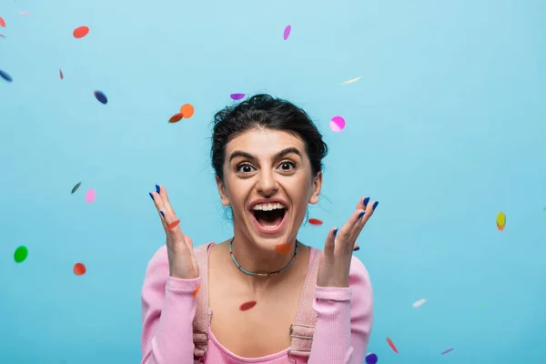 Overjoyed woman screaming and showing wow gesture under falling confetti isolated on blue — Stock Photo