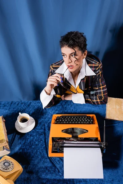 High angle view of vintage style newswoman near typewriter with blank paper on blue velour tablecloth — Stock Photo