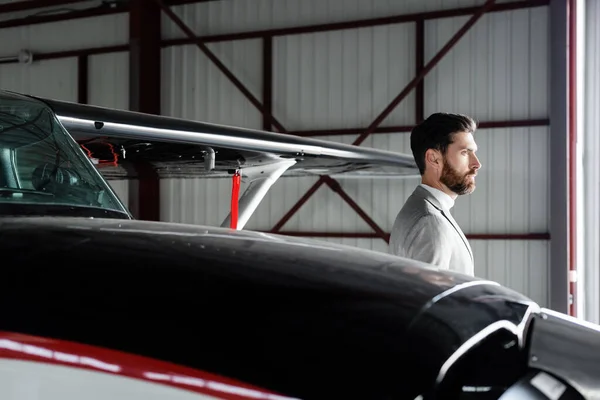 Bearded businessman in suit looking away near helicopter on parking — Stock Photo
