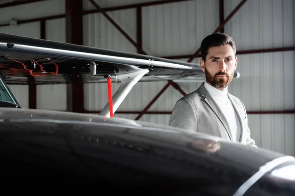 Bärtiger Geschäftsmann im Anzug schaut auf dem Parkplatz in die Kamera neben Hubschrauber — Stockfoto