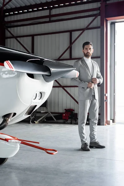 Full length of bearded man in suit buttoning blazer near helicopter — Stock Photo