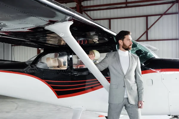 Confident bearded businessman in suit standing near modern helicopter — Stock Photo