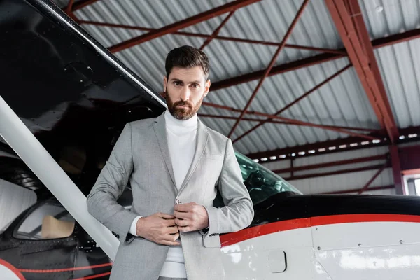 Low angle view of bearded businessman adjusting blazer near modern helicopter — Stock Photo
