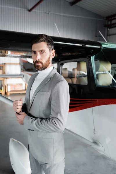 Confident bearded businessman in suit looking at camera near modern helicopter — Stock Photo