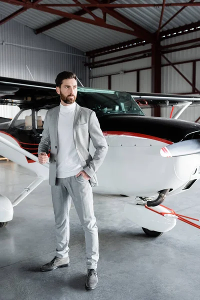 Longitud completa de hombre de negocios confiado en traje de pie con la mano en el bolsillo cerca de helicóptero moderno - foto de stock