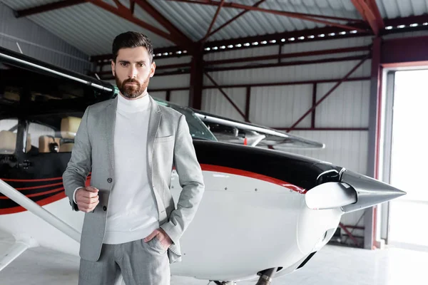 Homem de negócios barbudo confiante em terno de pé com a mão no bolso perto de helicóptero moderno — Fotografia de Stock